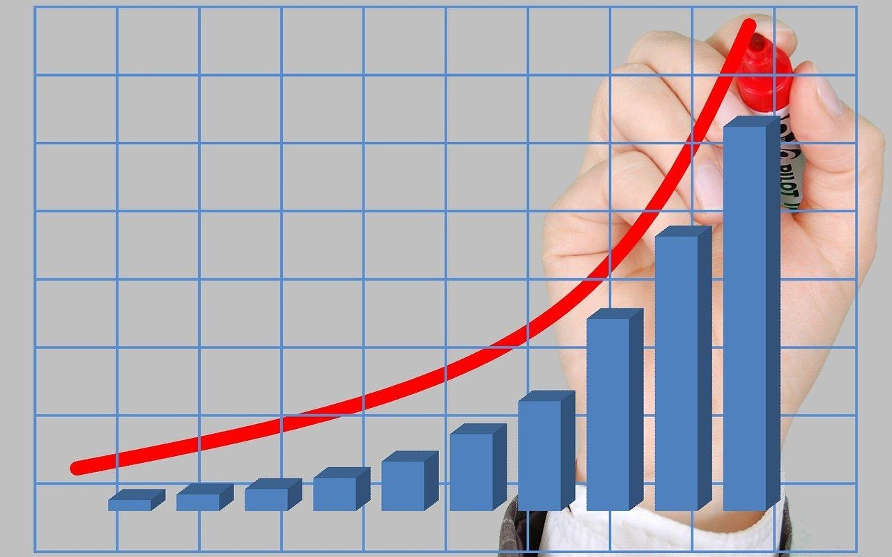 Hand drawing a red upward trend line on a bar graph with blue bars on a grid background.